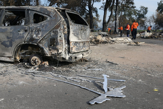 Search and rescue personnel inspect the aftermath of the Tubbs Fire behind a destroyed car in the Coffey Park neighborhood of Santa Rosa, California U.S., October 17, 2017.[Photo: VCG]
