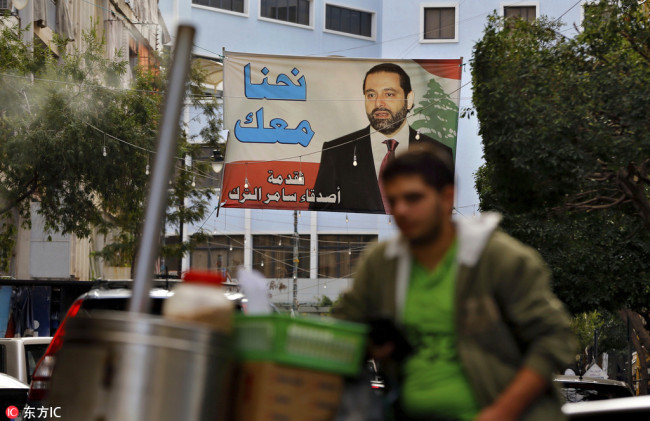 A street vendor stands in front of a poster of outgoing Prime Minister Saad Hariri that hangs on a street in Beirut, Lebanon, on Nov. 6, 2017. [Photo: IC]
