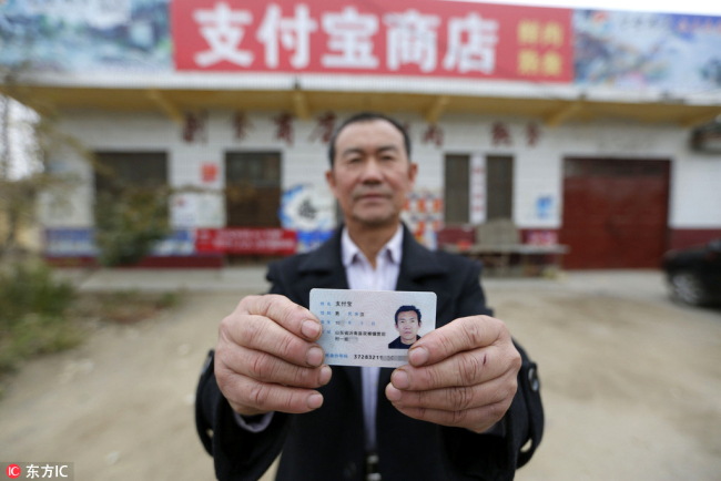 Zhi Fubao shows his identity card in front of his grocery store, November 17, 2017. [Photo: IC]