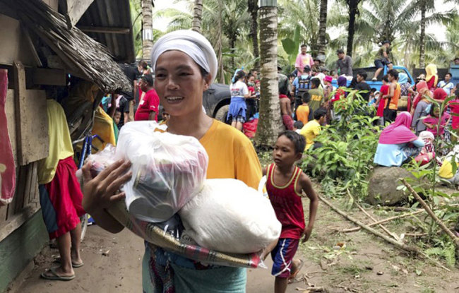 A resident smiles as she walks home with relief supplies being distributed to storm-affected villages of Lanao del Norte Sunday, Dec. 24, 2017 in southern Philippines. Tropical Storm Tembin unleashed flash floods that swept away people and houses and set off landslides in the southern Philippines. [Photo: AP] 