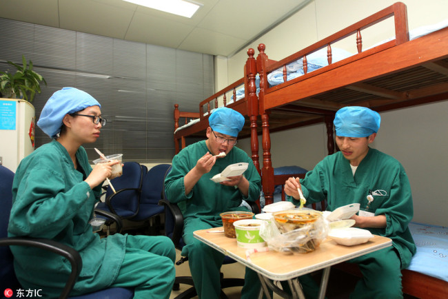 A female nurse (L) at a hospital in eastern Chinese province of Jiangsu has a late dinner with two male colleagues during a night shift  on March 16, 2015. [Photo: www.dfic.cn]