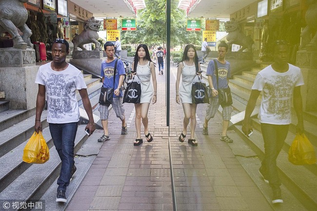 A young African man is reflected in the advertising billboard of a bus stop in Xiaobei district, which is known for its many wholesale markets in Guangzhou city, Guangdong Province on July 14, 2014. [File Photo: VCG] 