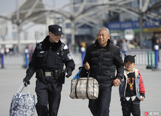 A policeman helps carry luggage for a senior citizen and a child at Fuyang Railway Station in Anhui Province on February 1, 2018. [Photo: IC]