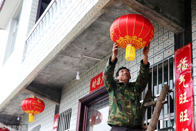 A farmer hangs lanterns in a village in Chongqing municipality on February 9, 2018. [Photo: VCG]