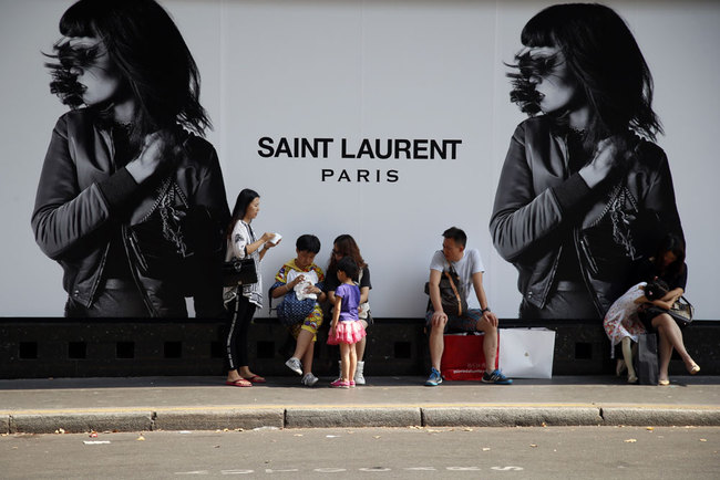 Chinese tourists take a rest during shopping outside a fashion store in Paris, France, Wednesday, Aug. 12, 2015. [Photo: AP]