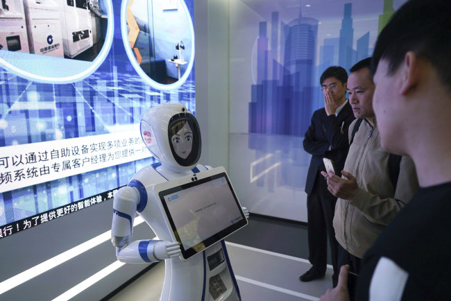 In this April 13, 2018, photo, bank customers speak with a robot at an automated branch in Shanghai. The outlet opened by Beijing-based China Construction Bank has been dubbed China's first "unmanned bank" and is equipped with face-scanning software, a virtual reality room and talking robots. [Photo: AP]