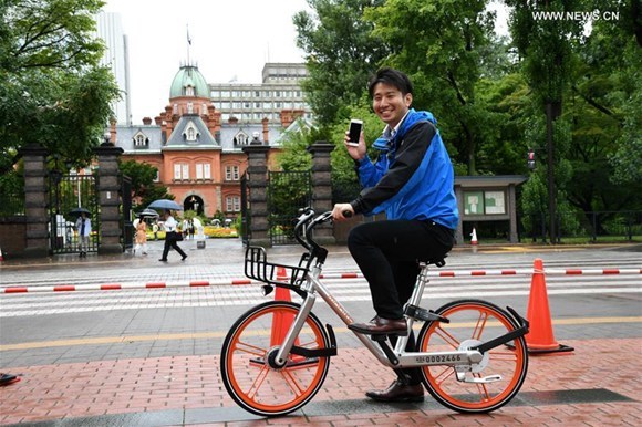 A TV reporter tries out a shared bicycle in Sapporo, Japan, on Aug. 22, 2017.[Photo: Xinhua/Hua Yi]