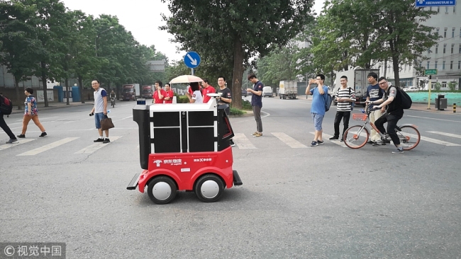 Pedestrians take photos of a JD.com automatic delivery vehicle as it crosses a road in Haidian District, Beijing, June 18, 2018. [Photo: VCG]