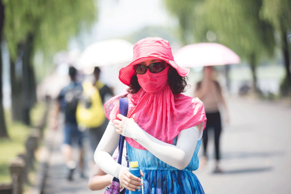A tourist wears hat, sunglasses, sunscreen masks and sleeves to escape the sun when she walks along the West Lake in Hangzhou, Zhejiang province. [Photo by Xu Kangping/Asianewsphoto]
