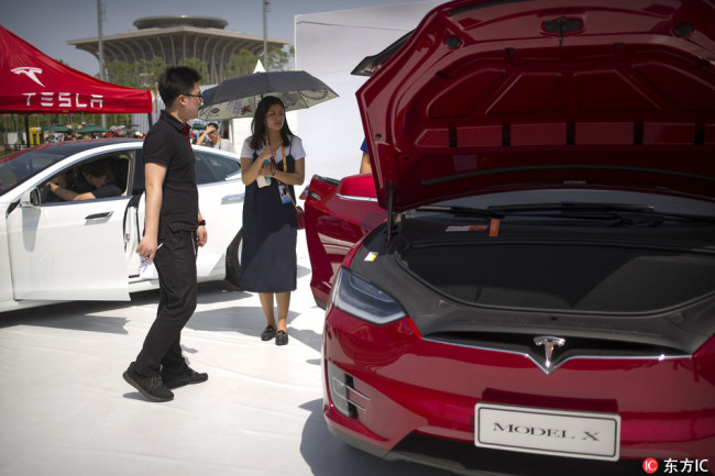 A visitor holds an umbrella as she looks at a Tesla Model X car on display at the G Festival, part of the Global Mobile Internet Conference (GMIC) in Beijing on April 29, 2017. [Photo: IC]