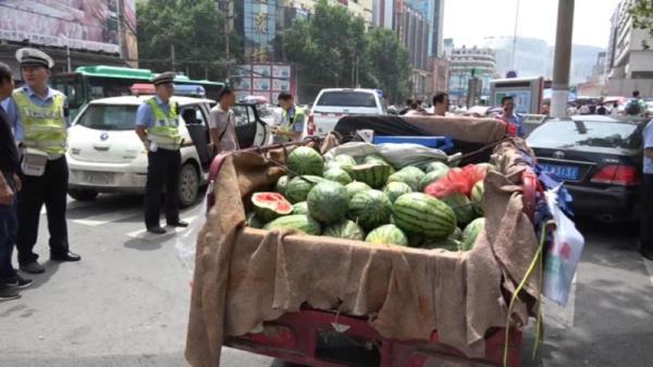 The watermelon vendor is stopped by traffic police officers for breaking the road rules in Zhengzhou, central China's Henan Province, on Saturday, July 14, 2018. [Photo: dahe.cn]
