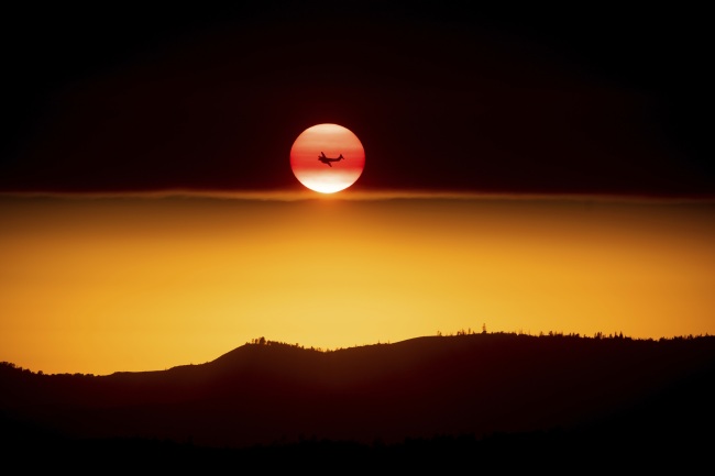 A plane battling the Ferguson Fire passes the setting sun in unincorporated Mariposa County Calif., near Yosemite National Park on Sunday, July 15, 2018. [Photo: AP/Noah Berger]