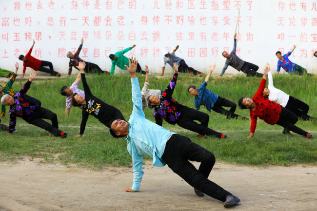 Lu Wenzhen, the first secretary of Yugouliang village, leads villagers to practice yoga. [Photo: China Daily/Zhu Xingxin]