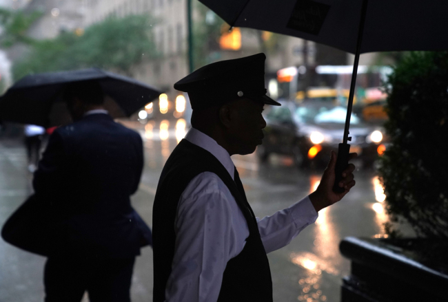 The doorman at Saks Fifth Avenue shields himself from the rain as remnants of Hurricane Florence hit the New York City area September 18, 2018. [Photo: AFP/Timothy A. Clary]