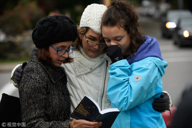 Tammy Hepps, Kate Rothstein and her daughter, Simone Rothstein, 16, pray from a prayerbook a block away from the site of a mass shooting at the Tree of Life Synagogue in the Squirrel Hill neighborhood on October 27, 2018 in Pittsburgh, Pennsylvania. [Photo: Getty Images/Jeff Swensen]