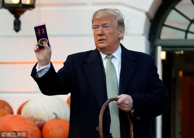 U.S. President Donald Trump holds up a Halloween candy with his signature on it before giving it to trick-or-treaters at the White House in Washington, U.S., October 28, 2018. [Photo: VCG]