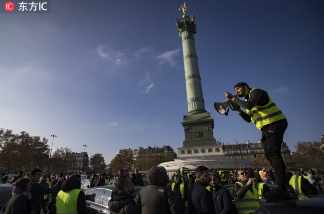 A man wearing a yellow high-visibility vest (mandatory in all vehicles in France) which has become a symbol of French driver's and citizen's protest against higher fuel prices, stands on a Uber car parked on Place de la Bastille as they try to block roads and cause traffic chaos as part of a nationwide protest, in Paris, France, November 17, 2018.[Photo: IC]