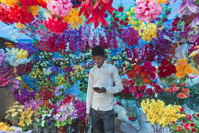 An Indian youth checks his phone as he sells plastic flowers at a local fair in Dharmsala, India, Sunday, Sept. 16, 2018. [Photo: AP]