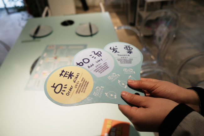 A hearing-impaired employee shows an order card and other tablets at the Forgive Hotpot Restaurant in Beijing on December 3, 2018. [File photo: IC]