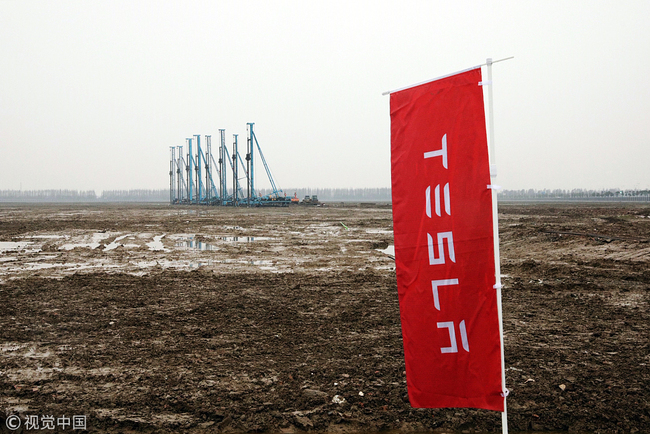 A banner stands in front of cranes at the site of the Tesla Inc. manufacturing facility in Shanghai, China, on Monday, Jan. 7, 2019. After four years of planning, Tesla finally broke ground on its planned $5 billion factory in the world's biggest auto market. [Photo: VCG/ Qilai Shen]