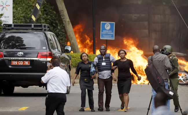 Security forces help civilians flee the scene as cars burn behind, at a hotel complex in Nairobi, Kenya, Jan. 15, 2019. [Photo: AP/Ben Curtis]