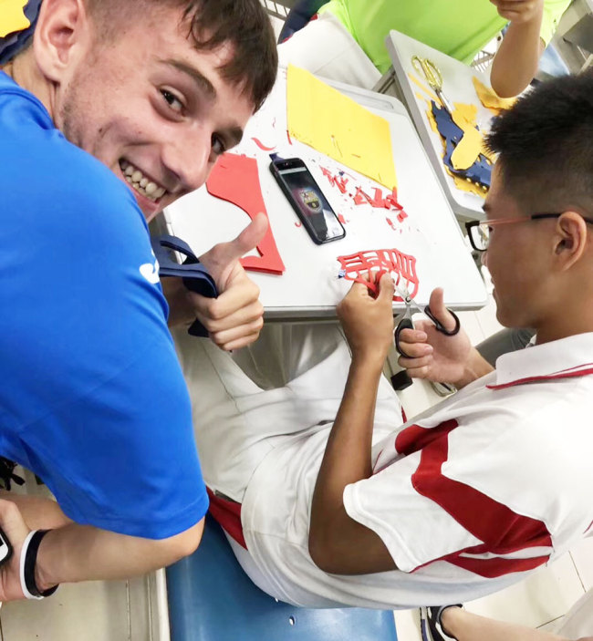 Li Yiran shows a Spanish student how to make paper-cutting of the FC Barcelona crest during a group of Spanish students' visit to the High School Affiliated to Renmin University of China. [Photo provided to China Plus]