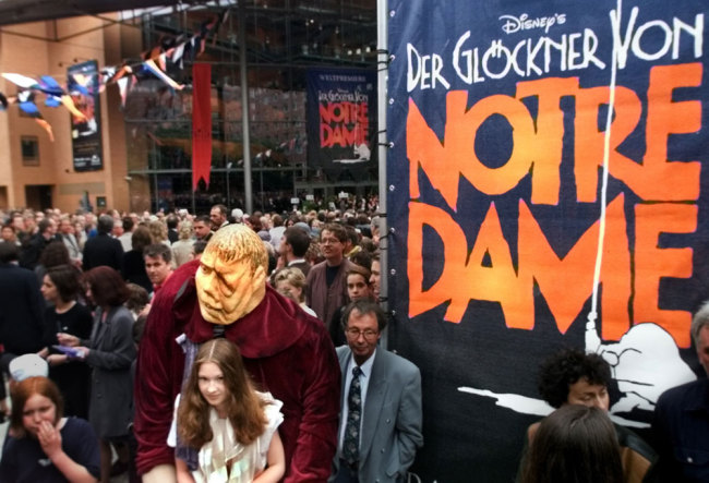 In this Saturday June 5, 1999 file photo, a girl dressed as Esmeralda carries a dummy of the character Quasimodo as people go into the new concert hall at Potsdamer Platz in Berlin, Germany, before the world premiere of the musical "The Hunchback of Notre Dame" later in the evening. The musical is a co-production of the U.S. American Disney company and the German musical company Stella. [File photo: AP/Jan Bauer]