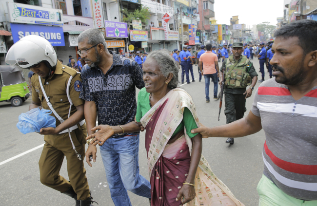 Sri Lankan elderly woman is helped near St. Anthony's Shrine after a blast in Colombo, Sri Lanka, on April 21, 2019. [Photo: AP/Eranga Jayawardena]