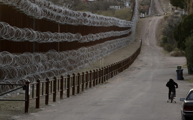 A boy rides his bike along a razor-wire-covered border wall that separates Nogales, Ariz., from Nogales, Mexico on the other side Saturday, March 2, 2019. [File photo: AP]