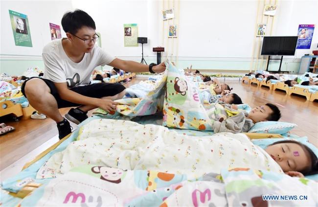 Chen Xuliang, a teacher in his 20s, covers children with quilts at a kindergarten in Yangzhou, Jiangsu Province, September 4, 2018. [Photo: Xinhua]