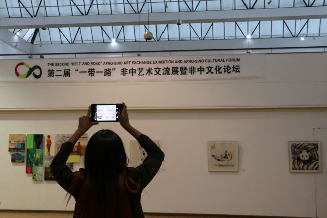 A visitor takes a picture of the art works displayed at the Second Belt and Road Afro-Sino Art Exhibition launched by the National Gallery of Zimbabwe on Monday, April 29, 2019. [Photo: China Plus/Gao Junya]