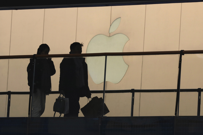 In this Jan. 3, 2019, file photo, shoppers pass by the Apple store logo at a shopping mall in Beijing. Apple Inc. reports financial results Tuesday, April 30. [File Photo: AP/Ng Han Guan]