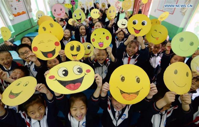 Pupils(学生们 xuéshēngmen) demonstrate smiley cards(卡片 kǎpiàn) to greet the upcoming World Smile Day at a primary school in Handan, north China's Hebei Province, May 7, 2019. [Photo: Xinhua]