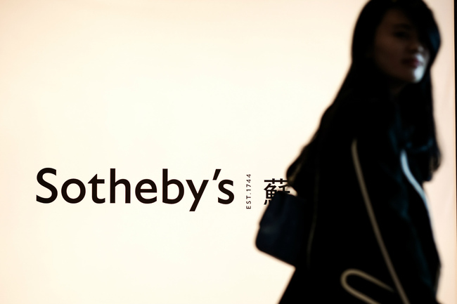 FILE - In this file photo taken on October 5, 2012 a woman walks past an illuminated board of the Sotheby's logo in Hong Kong. French billionaire Patrick Drahi says on June 17, 2019 he acquires Sotheby's auction house in $3.7 bn deal. [Photo：AFP/Philippe LOPEZ]