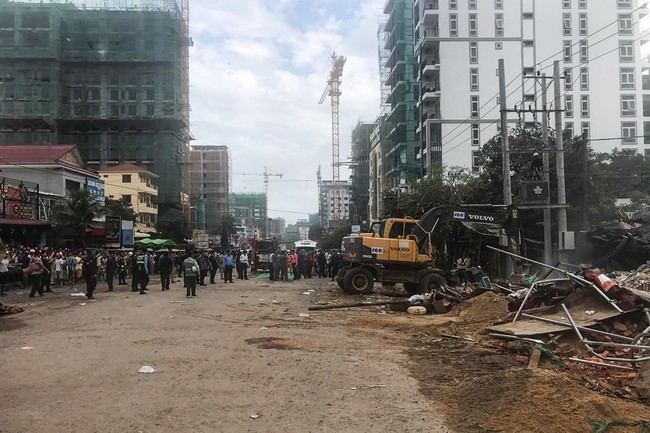 People watch as rescue workers use an earthmover to clear debris after an under construction building collapsed in Sihanoukville on June 22, 2019. [Photo: AFP]