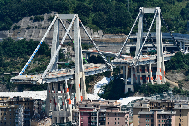 A general view shows the two pylons of Genoa's Morandi motorway bridge seen in red on the structure below, on June 27, 2019 in Genoa. Some of the remains of Genoa's Morandi motorway bridge were destroyed on June 28, 2019, almost eleven months after its partial collapse during a storm killed 43 people and injured dozens. [Photo: AFP/Vincenzo Pinto]