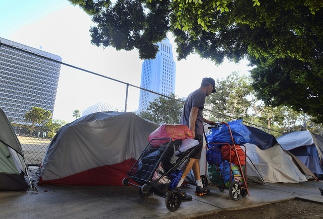 In this Monday, July 1, 2019 photo, a homeless man moves his belongings from a street behind Los Angeles City Hall as crews prepared to clean the area. [Photo: AP/Richard Vogel]