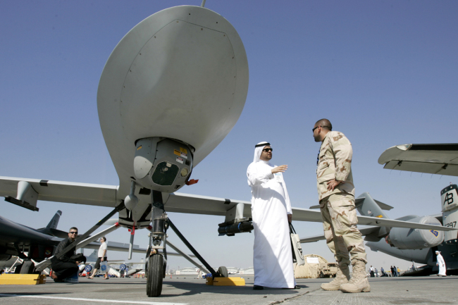 A visitor asks questions to a U.S. military representative, as they stand next to an MQ-1 Predator spy plane, during the 10th Dubai Airshow, at the Dubai airport, United Arab Emirates. [File Photo: IC]