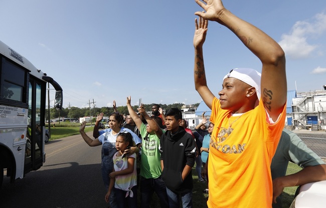 Friends, coworkers and family wave to one of several buses that are filled with detainees, following a U.S. Immigration raid at several Mississippi food processing plants, including this Koch Foods Inc., plant in Morton, Miss., Wednesday, Aug. 7, 2019. [Photo: AP/Rogelio V. Solis]