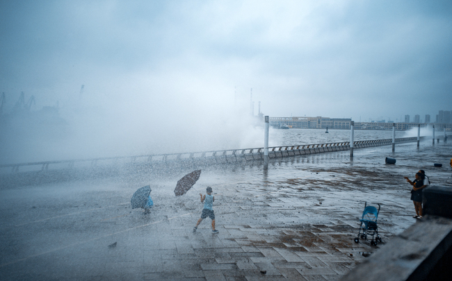 People watch huge waves from a tidal bore caused by Typhoon Lekima, surging past a barrier on the banks along the seacoast in Dalian, Liaoning Province, August 12, 2019. [Photo: IC]