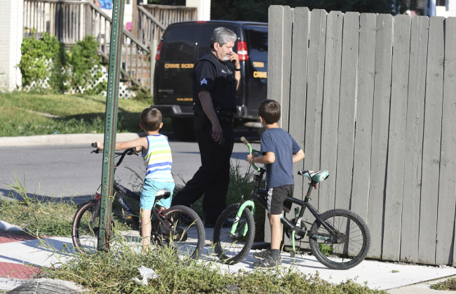 Two boys watch as a Detroit police officer investigates a fatal dog attack on a young girl who later died of her injuries in Detroit on Monday, Aug. 19, 2019. Police say the owner of three dogs is in custody after the animals killed Emma Hernandez, 9, as she rode a bike. The girl's father, Armando Hernandez, says the man was warned that a fence was too flimsy to hold the dogs. [Photo: Max Ortiz/Detroit News via AP]