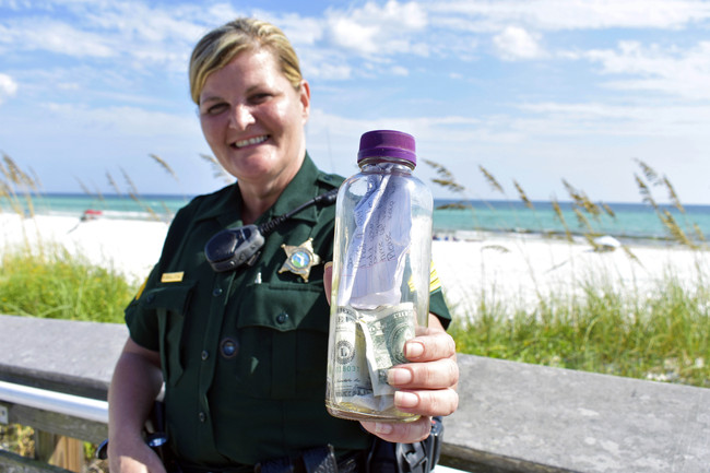 In this undated photo provided by the Walton County Sheriff's Office Sgt. Paula Pendleton poses with a bottle that washed ashore last week near Miramar Beach, Fla. A bottle containing the ashes of a Texas man along with some handwritten notes from loved ones has been returned to the Gulf of Mexico, resuming its ocean journey after it washed up on a Florida Panhandle beach. [Photo: AP/Corey Dobridnia/Walton County Sheriff’s Office]