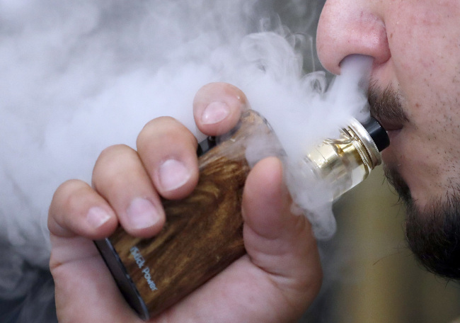 In this Friday, Aug. 17, 2018 file photo, a man breathes vapes from an e-cigarette at a vape shop in London. [File Photo: AP/Frank Augstein]
