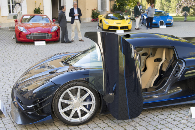 People looking at a 2015 Koenigsegg One:1 model car in front of a Aston Martin One-77 Coupe (2011), red, Ferrari LaFerrari (2015), yellow, and a Bugatti Veyron EB 16.4 Coupe (2010), blue, part of some 25 luxury cars owned by Teodoro Obiang, the son of the Equatorial Guinea's President Teodoro Obiang Nguema Mbasogo are pictured before an auction of sales house Bonhams at the Bonmont Abbey Golf & Country Club in Cheserex near Geneva, Switzerland, Sunday, September 29, 2019. [Photo: Laurent Gillieron/Keystone via AP]