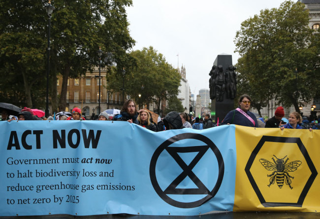 Climate change activists from the Extinction Rebellion block the road with a banner that calls on the government to act now to reduce greenhouse gas emissions to halt biodiversity loss on Whitehall outside Downing Street in central London, on October 7, 2019 during the group's global climate protests. [Photo: AFP]