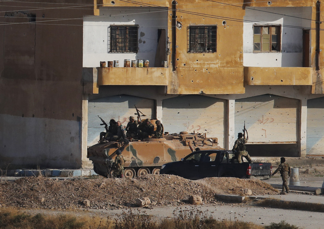 In this photo taken from the Turkish side of the border between Turkey and Syria, in Akcakale, Sanliurfa province, southeastern Turkey, Turkish-backed Syrian opposition fighters advance with theirs armoured personnel carrier in Tel Abyad, Syria, Sunday, Oct. 13, 2019. [Photo: AP/Lefteris Pitarakis]