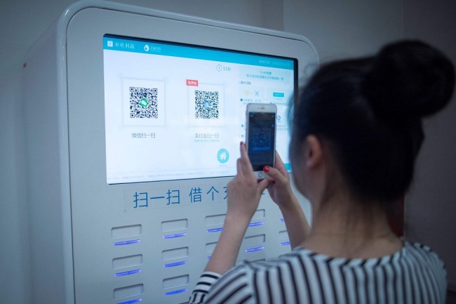 This picture taken on July 5, 2017 in Shanghai shows a woman scanning a QR code on a shared battery station inside a shop. [File Photo: VCG]