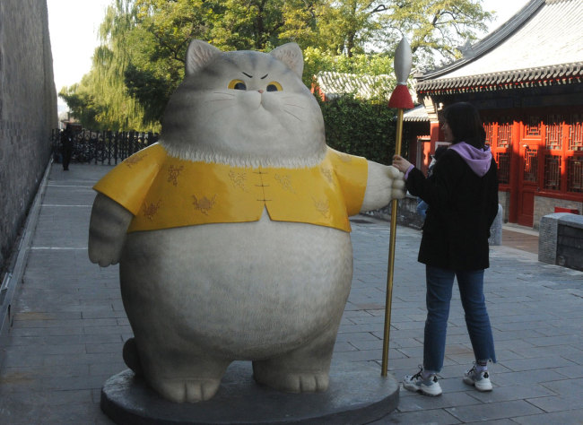 Tourists take photos with the cat statues near the Palace Museum Online Shopping Gallery in Beijing on Monday, October 28, 2019. [Photo: VCG]