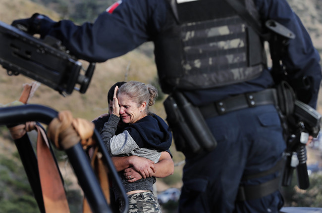 Framed by heavily armed Mexican authorities, relatives of the LeBaron family mourn at the site where nine U.S. citizens, three women and six children related to the extended LeBaron family, were slaughtered when cartel gunmen ambushed three SUVs along a dirt road near Bavispe, at the Sonora-Chihuahua border, Mexico, Wednesday, Nov 6, 2019. [Photo: AP]