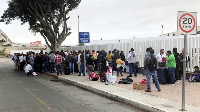 Asylum seekers in Tijuana, Mexico, listen to names being called from a waiting list to claim asylum at a border crossing in San Diego, Sept. 26, 2019. [Photo: AP/Elliot Spagat]